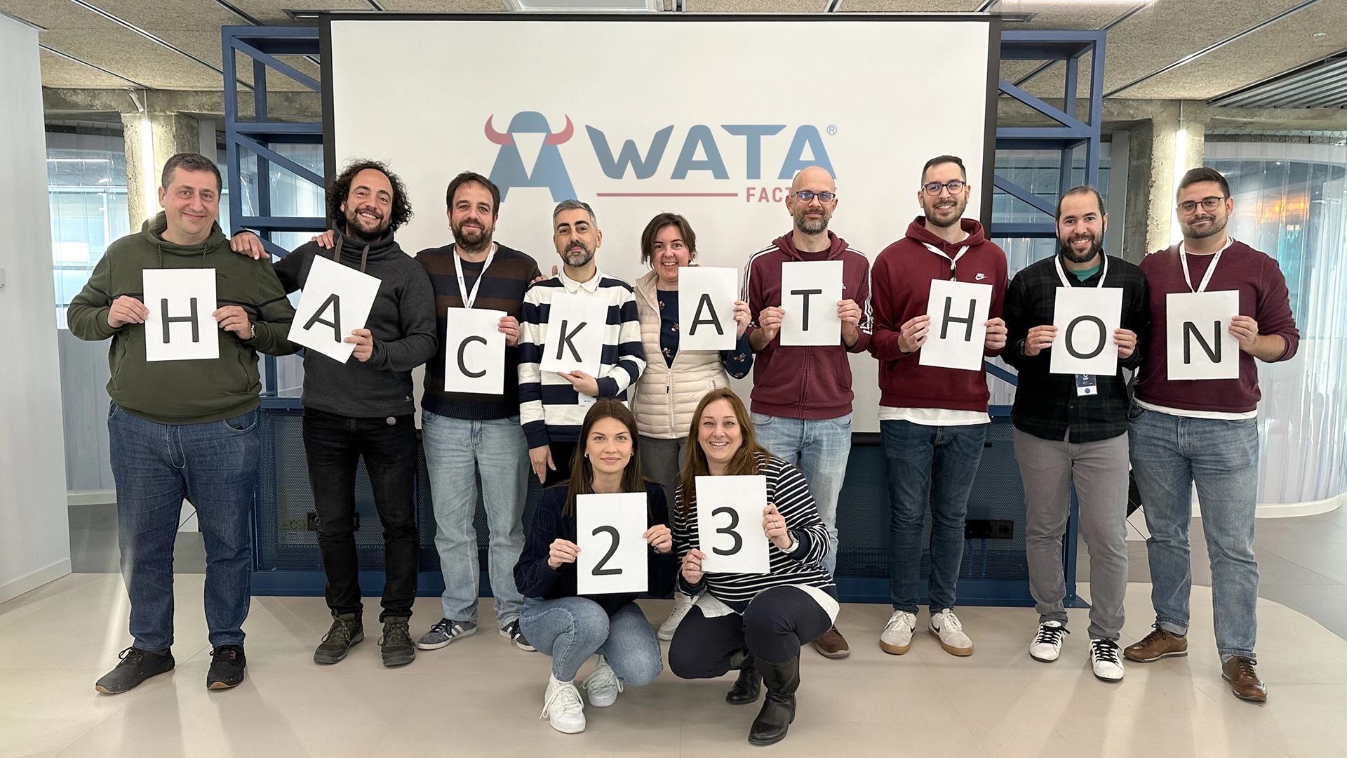 Team hält Buchstaben, die "HACKATHON 23" vor dem WATA Factory-Logo bilden