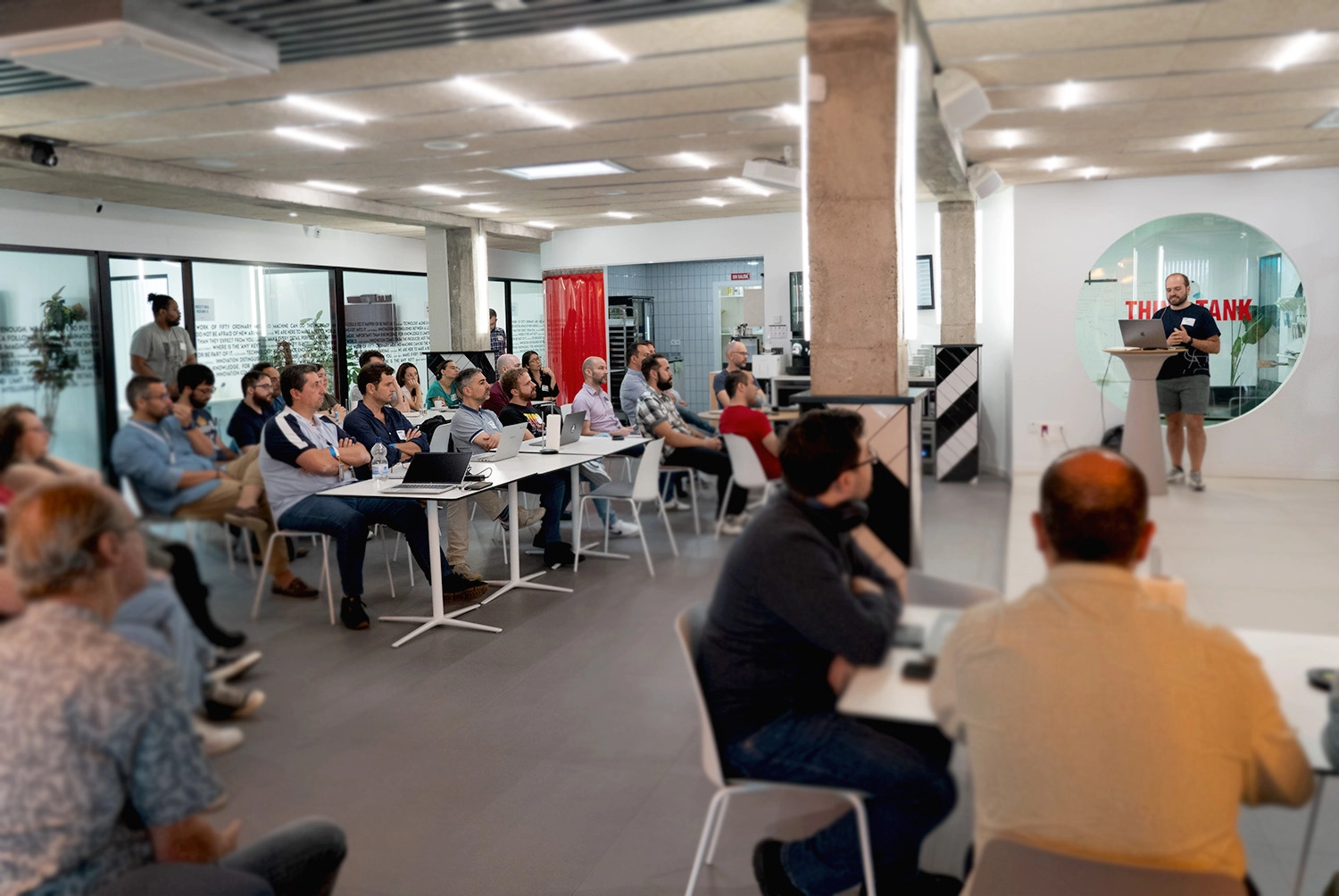 Publikum in modernem Büroraum, das einen Vortrag des stehenden Redners verfolgt