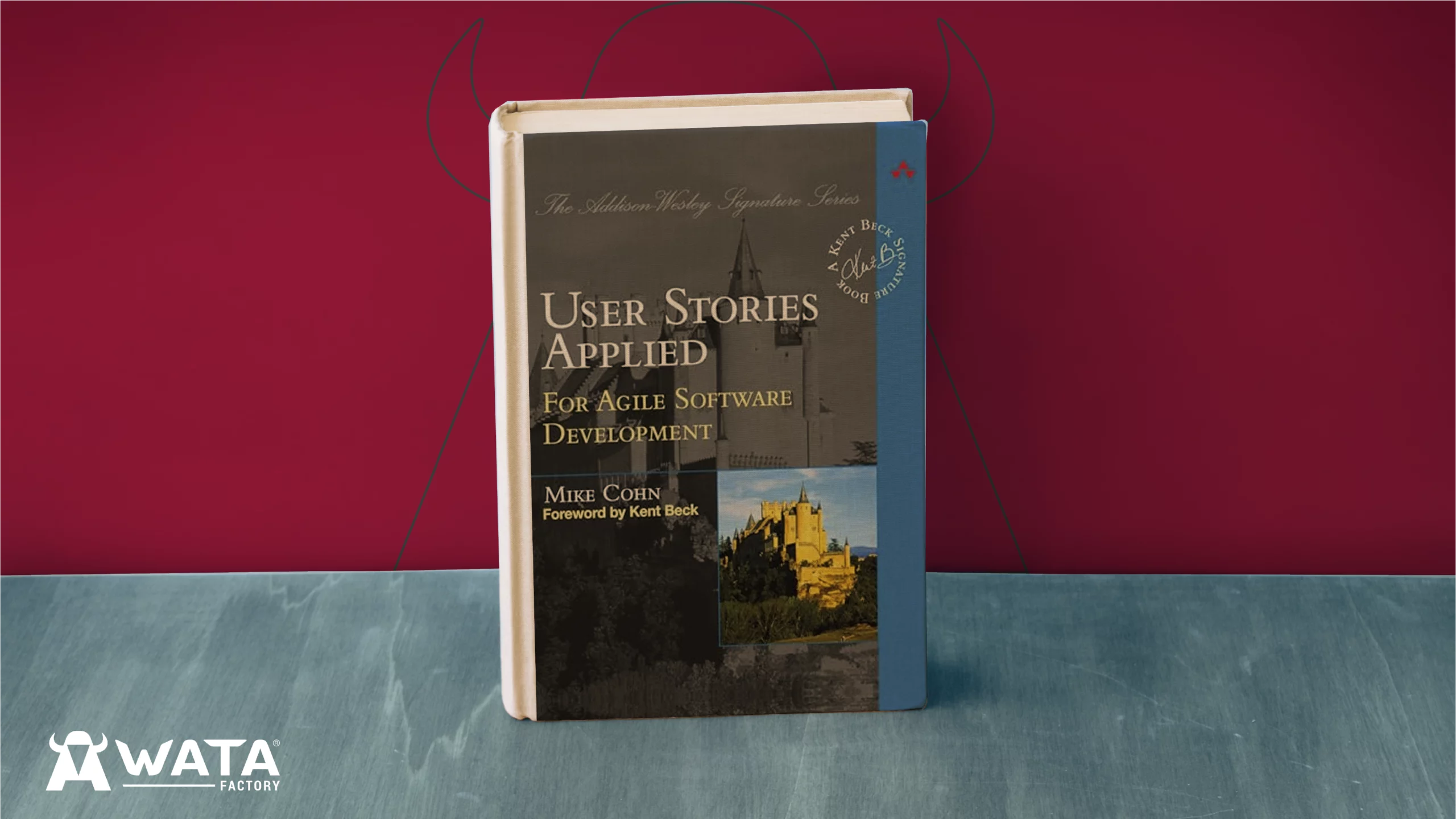 Portada del libro User Stories Applied de Mike Cohn, colocado sobre un fondo con los colores corporativos de WATA Factory y el logo de la empresa visible detrás.