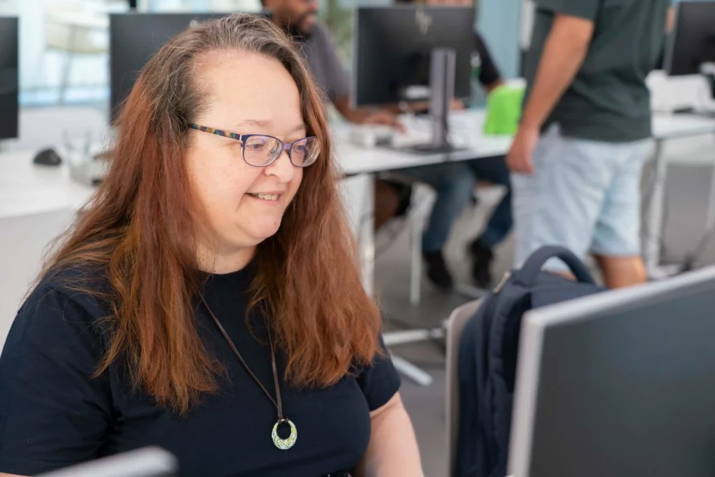 WATA Factory employee smiling and focused on her laptop during the Kubernetes workshop.