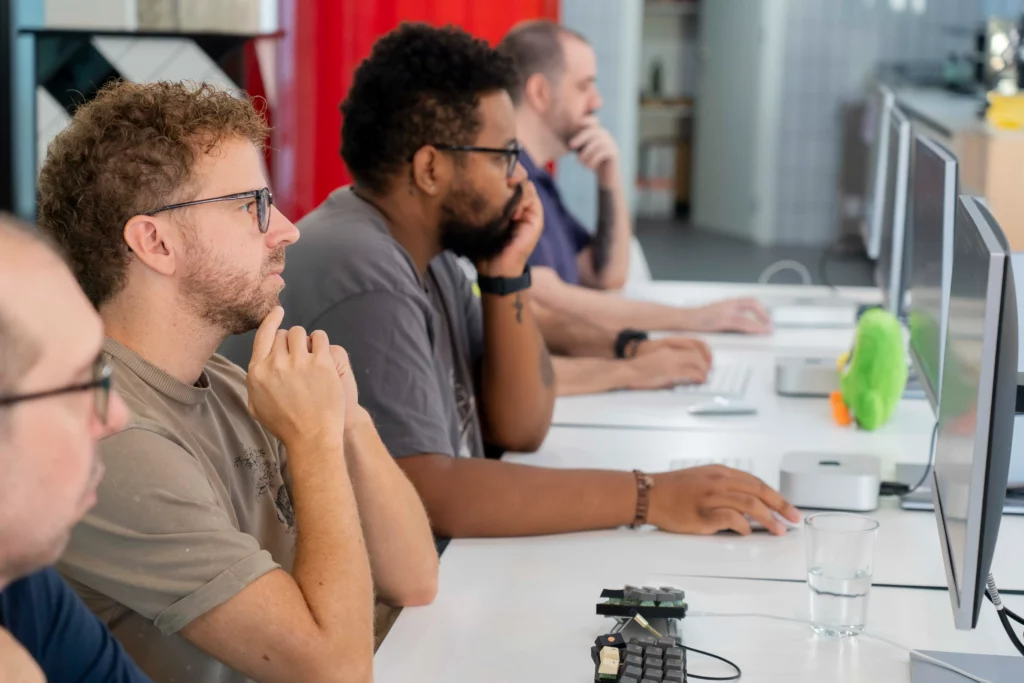 Reihe von Tischen mit WATA Factory-Mitarbeitern, die an Laptops arbeiten und den Anweisungen von Laura Morillo-Velarde zu Kubernetes folgen.