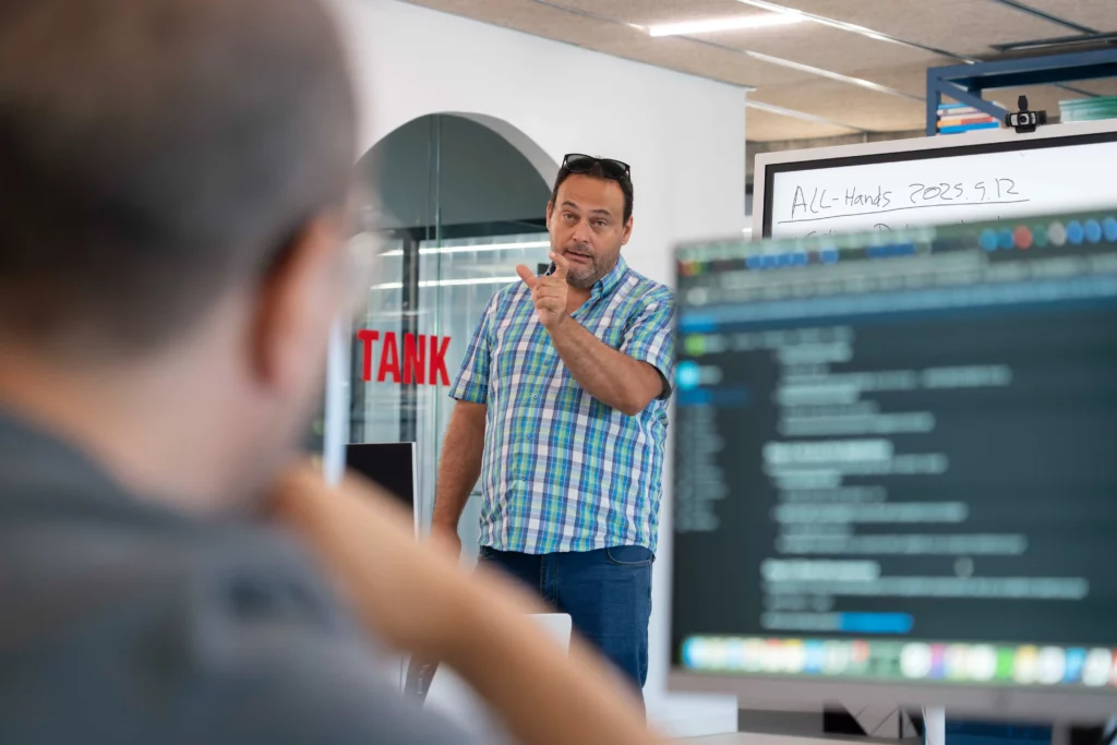 View from an employee’s laptop towards Pedro G. answering questions about DevOps and Kubernetes.