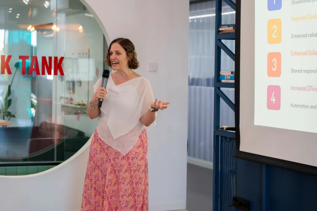 Laura Morillo-Velarde on stage at WATA Factory presenting on Kubernetes and DevOps with slides projected.