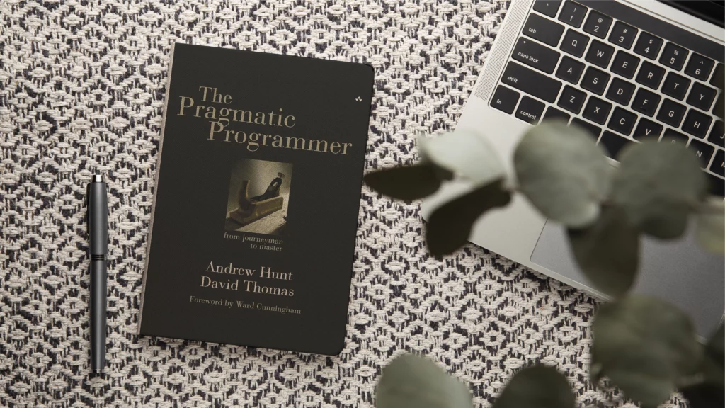 The Pragmatic Programmer Buchcover neben einem Laptop – Klassiker Entwicklerbuch 2026 über Best Practices und Problemlösung.