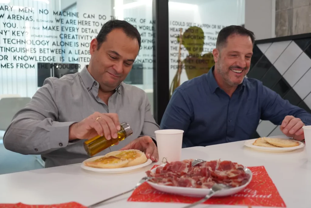 Two colleagues smiling while preparing mollete toast during the Andalusian breakfast at the Christmas All Hands.