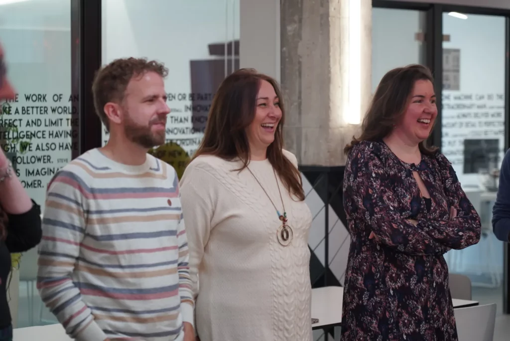 Three colleagues smiling while listening to the personalised Christmas carol at the All Hands.