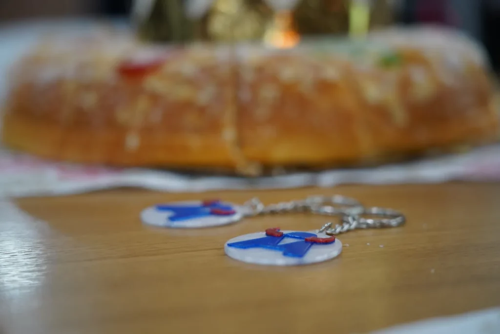 Two 3D-printed WATA Factory keychains placed next to a traditional Three Kings cake.