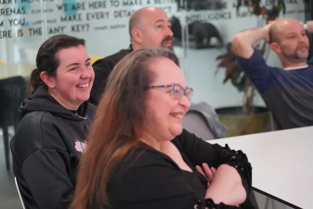 Two WATA Factory colleagues smiling while listening to Iberica Labs presentations about development and testing.