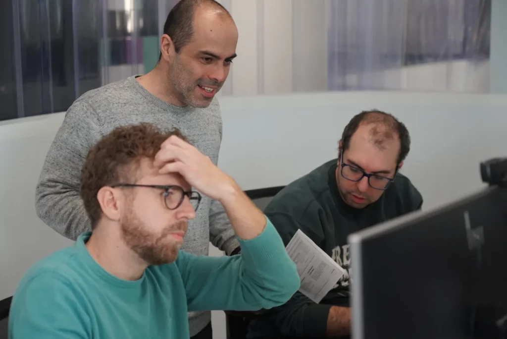 Three colleagues collaborating at a computer during Iberica Labs while exploring improvements in automated testing.